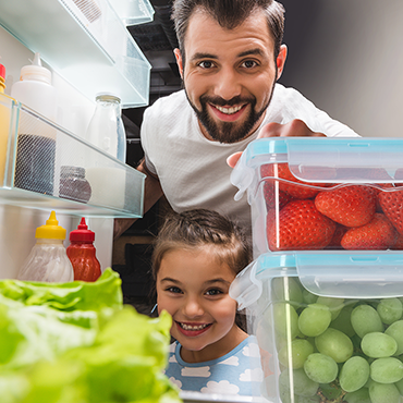 Tochter und Papa suchen im Kühlschrank nach frischen Erdbeeren.